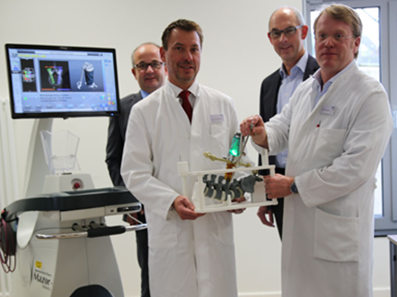 Die beiden Wirbelsäulenchirurgen Dr. Gregory Köppen und Dr. Carsten Schneekloth mit dem Roboter (grün leuchtendes Gerät) an einem Modell der Wirbelsäule
