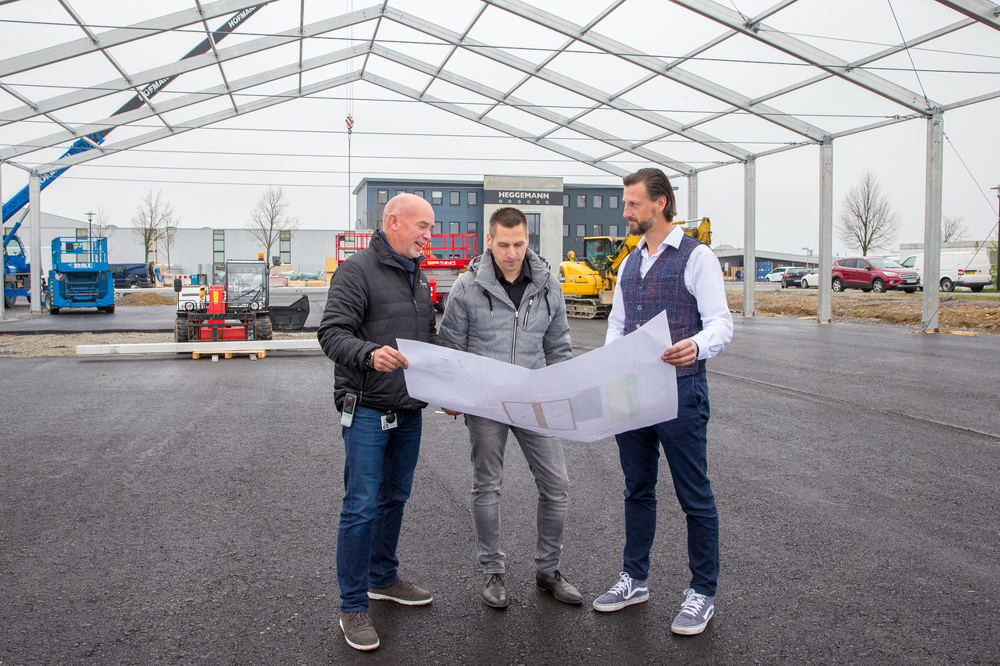 Drei Männer stehen in einer Halle und schauen auf einen Bauplan.