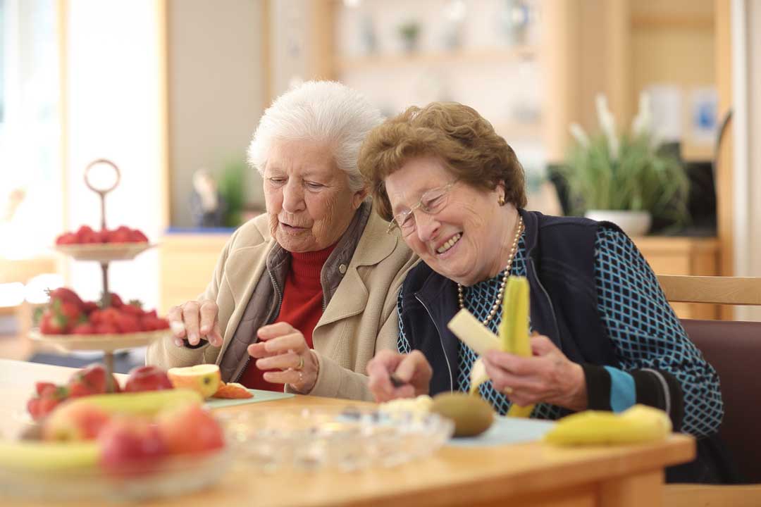 Zwei Seniorinnen sitzen fröhlich zusammen.