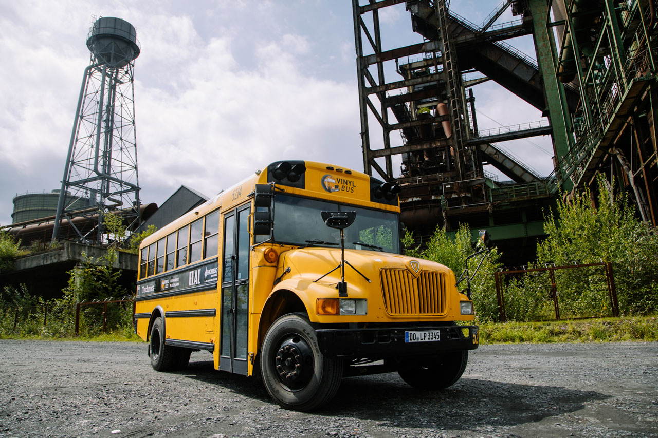 Der Vinylbus vor einer Industrieanlage.