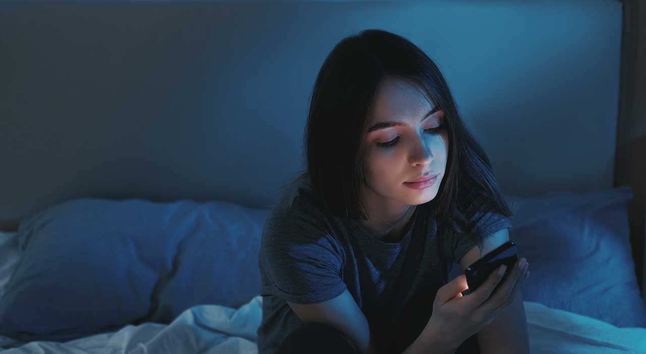 Mädchen mit Smartphone im Bett sitzend.