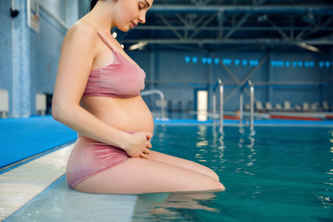 Schwangere sitzt am Beckenrand und bereitet sich zur Wassergymnastik vor.